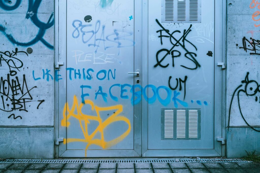 Graffiti "Like this on Facebook" na zniszczonych metalowych drzwiach, symbolizujące minioną erę "starego Facebooka" i jego wpływ na kulturę.